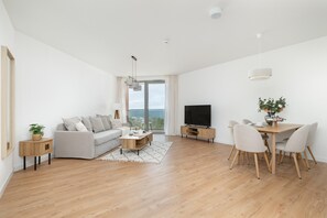 A modern living room with a sofa, coffee table, TV, dining table with chairs, and a large window with a view. - Apartment With Direct sea View (Rewal)