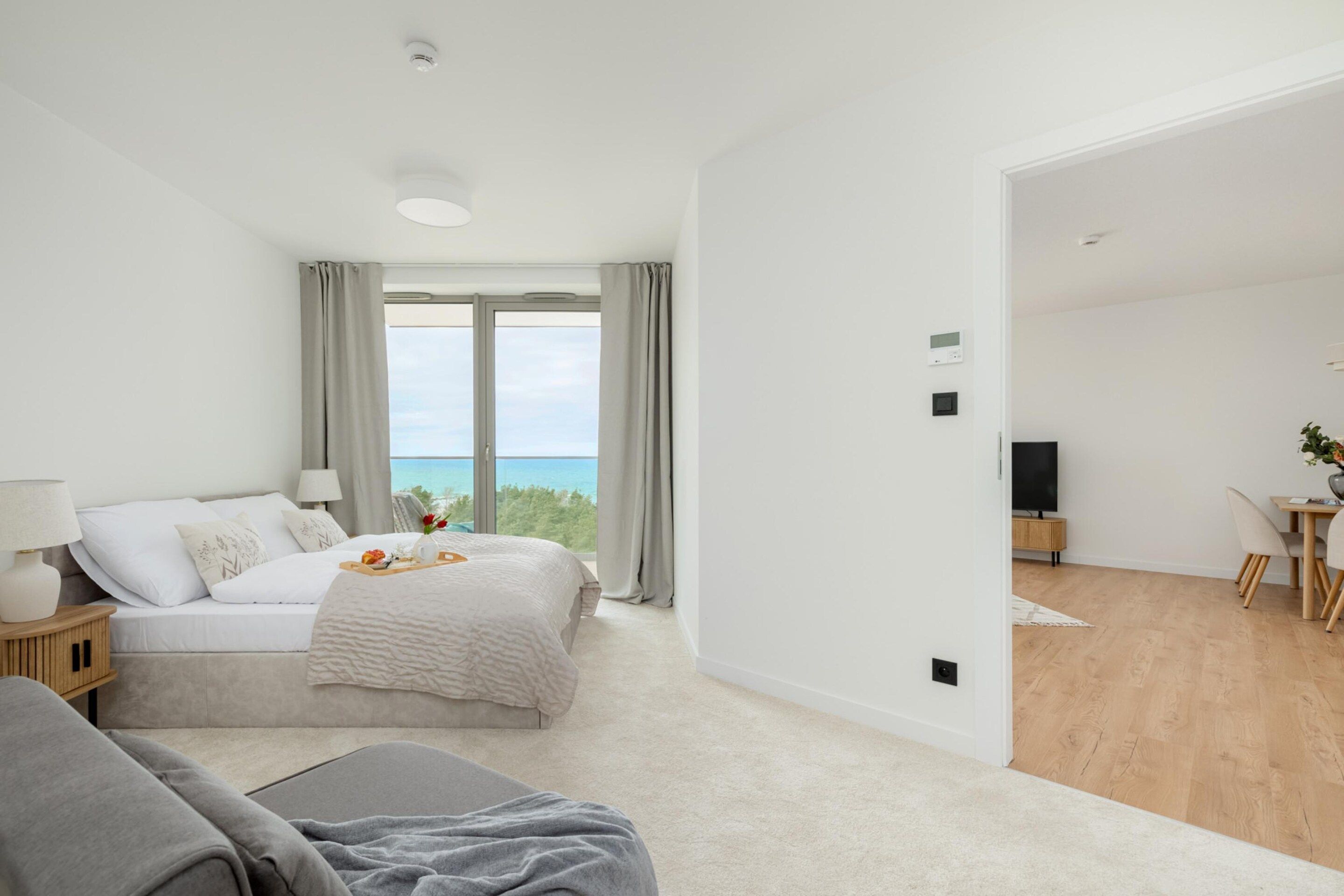 A modern bedroom with a bed, bedside table, and a view of the sea.