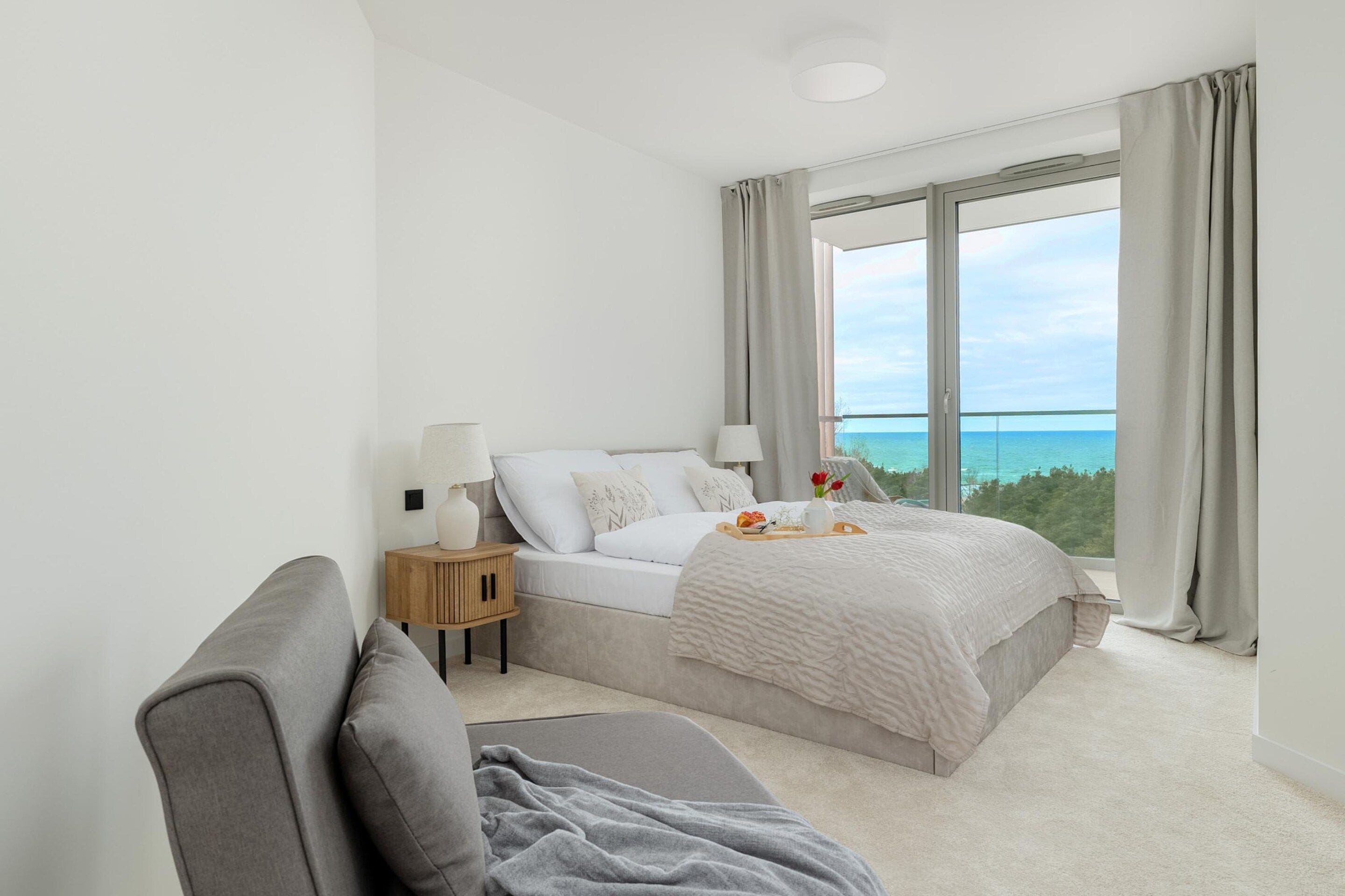 A bedroom with a bed, bedside tables, a view of the ocean, and a balcony.