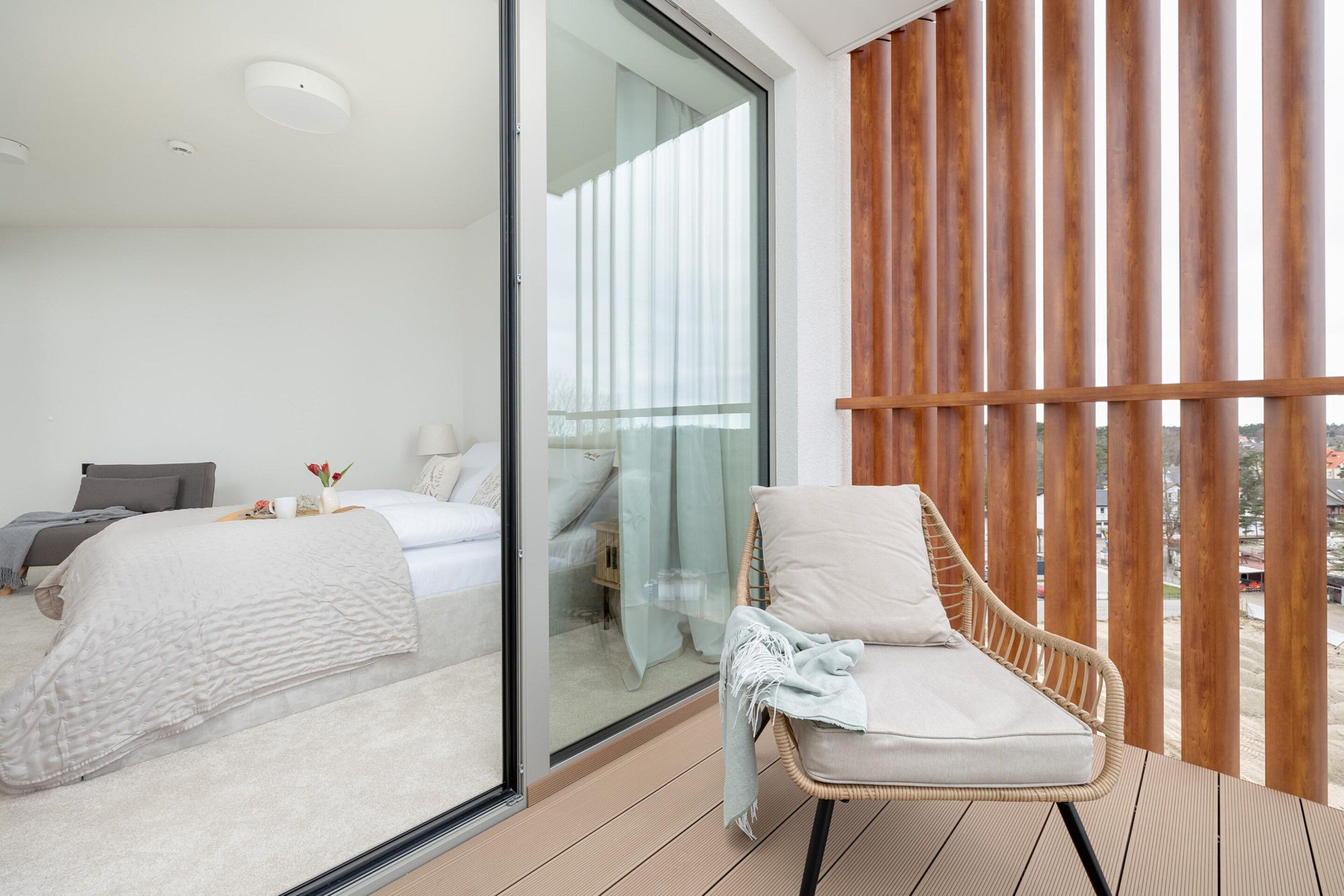 Ein modernes Schlafzimmer mit Glaswand, einem Bett, einem Sessel und Blick ins Freie.