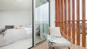 Ein modernes Schlafzimmer mit Glaswand, einem Bett, einem Sessel und Blick ins Freie.