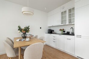 A modern kitchen with white cabinets, a wooden dining table, and a vase with flowers. - Apartment With Direct sea View (Rewal)