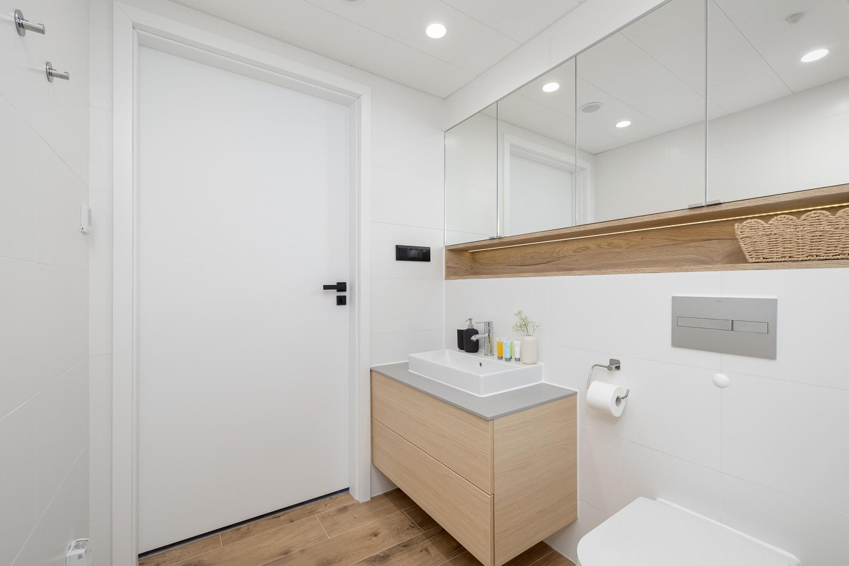 Un bagno moderno con una porta bianca, un mobile bagno in legno, uno specchio e un water.