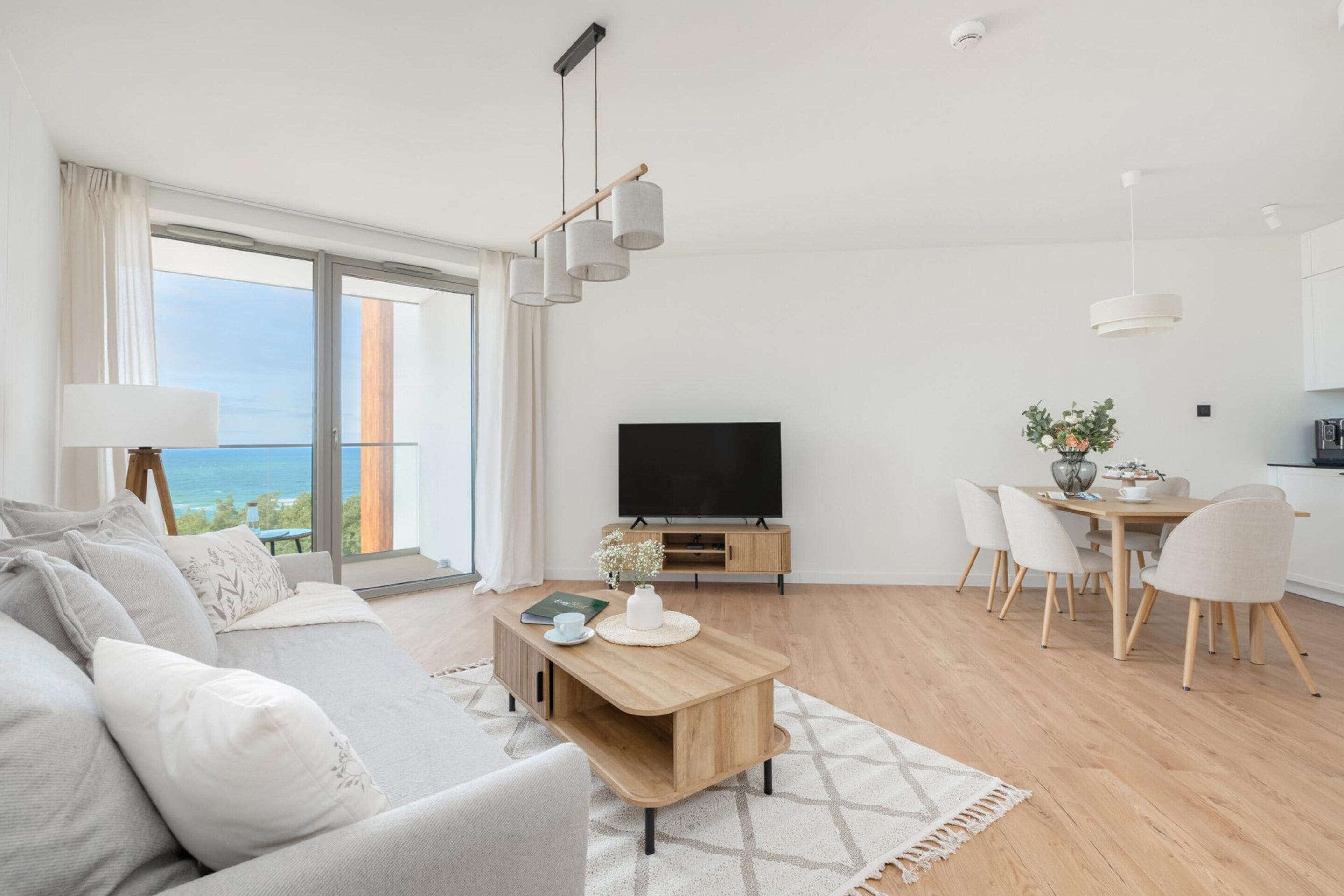 Ein modernes Wohnzimmer mit einer Couch, einem Couchtisch und einem Fernseher. Es gibt einen Essbereich mit Tisch und Stühlen.