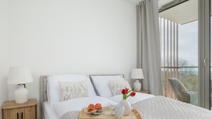 A hotel room with a bed, two bedside tables, a window with curtains, and a view of the outdoors. - Apartment With Direct sea View (Rewal)