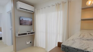 A modern living room with a flat-screen TV mounted on the wall, a built-in air conditioning unit, a white curtain, and a marble countertop. - Solarium Beach Club - Apartamento T1.706 (Itapoá)