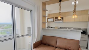 A modern kitchen with wooden cabinets, a built-in oven, and a hanging light fixture. - Solarium Beach Club - Apartamento T1.706 (Itapoá)