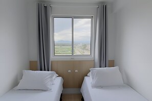 Une chambre d’hôtel avec deux lits simples, une grande fenêtre donnant sur un paysage et une tête de lit en bois.