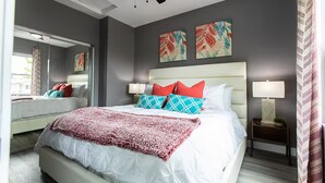 Ein modernes Schlafzimmer mit einem großen Bett, zwei Nachttischen mit Lampen, einem Deckenventilator und Kunstwerken an den Wänden.