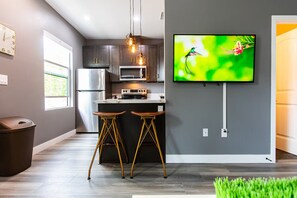 A modern kitchen with a built-in oven, microwave, and stainless steel refrigerator. There are two stools and a trash bin. - Bright King Suite Near Dining, Shops & Parks (San Diego)