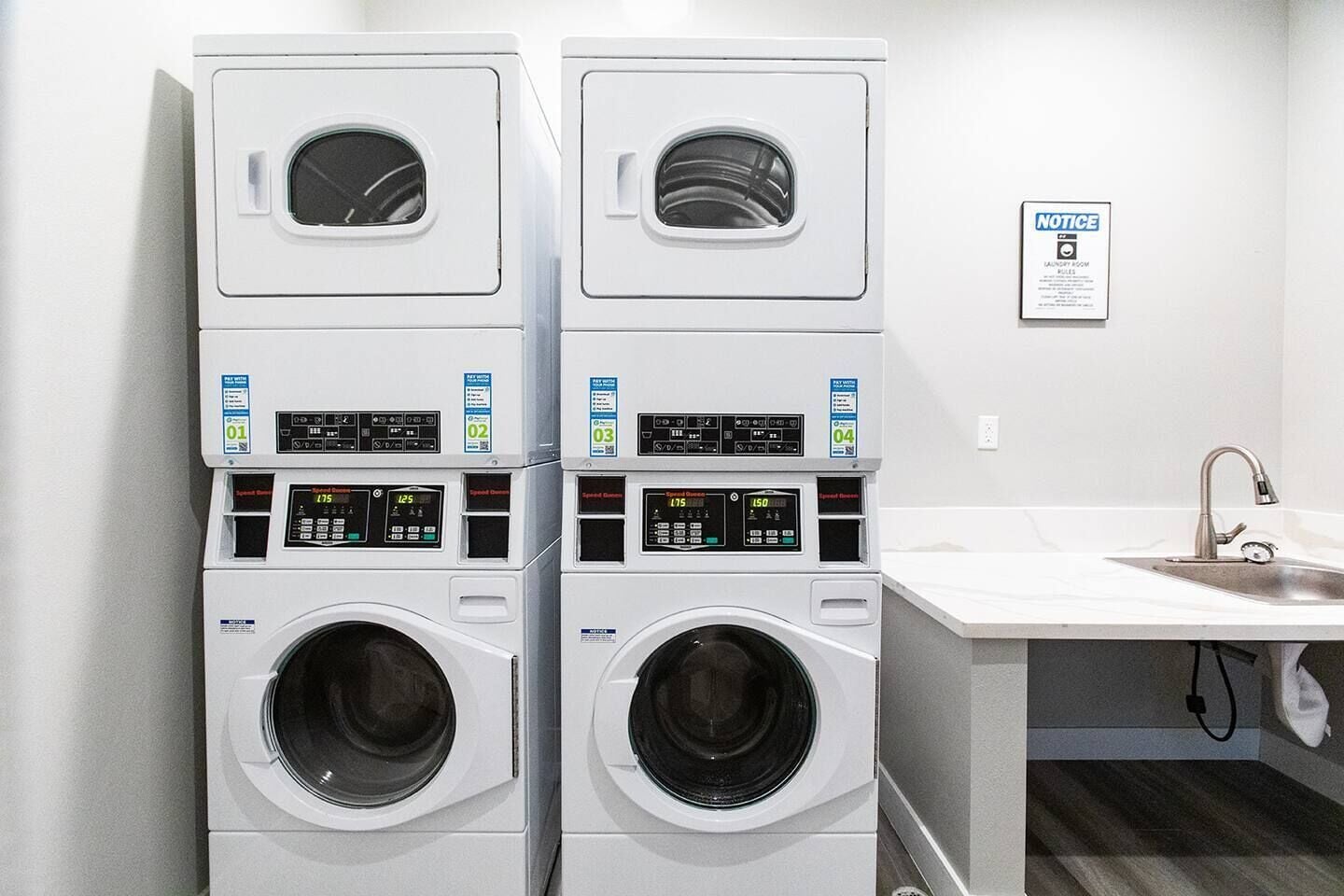 A laundry room with four stacked front-loading washing machines and a sink.