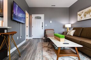 A modern living room with a grey wall, a flat-screen TV, a brown sofa, a patterned rug, and a wooden coffee table. - Bright King Suite Near Dining, Shops & Parks (San Diego)