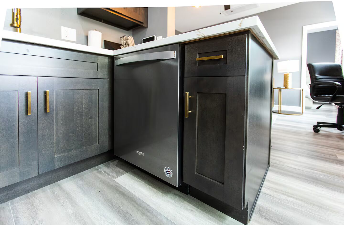 A modern kitchen with dark cabinetry, stainless steel appliances, and a light wood floor.