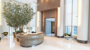 A modern lobby with a reception desk, a large indoor tree, and a spacious area with a high ceiling and large windows. - Vogue| Opera Grand near Dubai Mall | Burj Khalifa (Dubai)