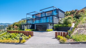 A modern two-story house with large glass windows, a driveway, and landscaped gardens. - Luxury Bay Retreat in Kaiteriteri (Kaiteriteri)