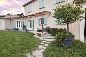 A two-story house with a covered patio, a small garden, and a stone pathway leading to the entrance. - "LES LOUVETTES" in the heart of the countryside. (Châteaurenard)
