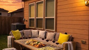 A backyard with a wooden house, a wicker sofa set, a dining table with food and drinks, and a covered grill. - Spacious 5BR Retreat Sleeps 13 Premium Bedding Near NRG & Events (Houston)