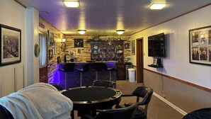 A room with a bar area, a round table, and several chairs. There are framed pictures on the walls and a television mounted on the wall. - Cozy 1-bedroom 1st floor in beautiful Pittsburgh with AC (Pittsburgh)