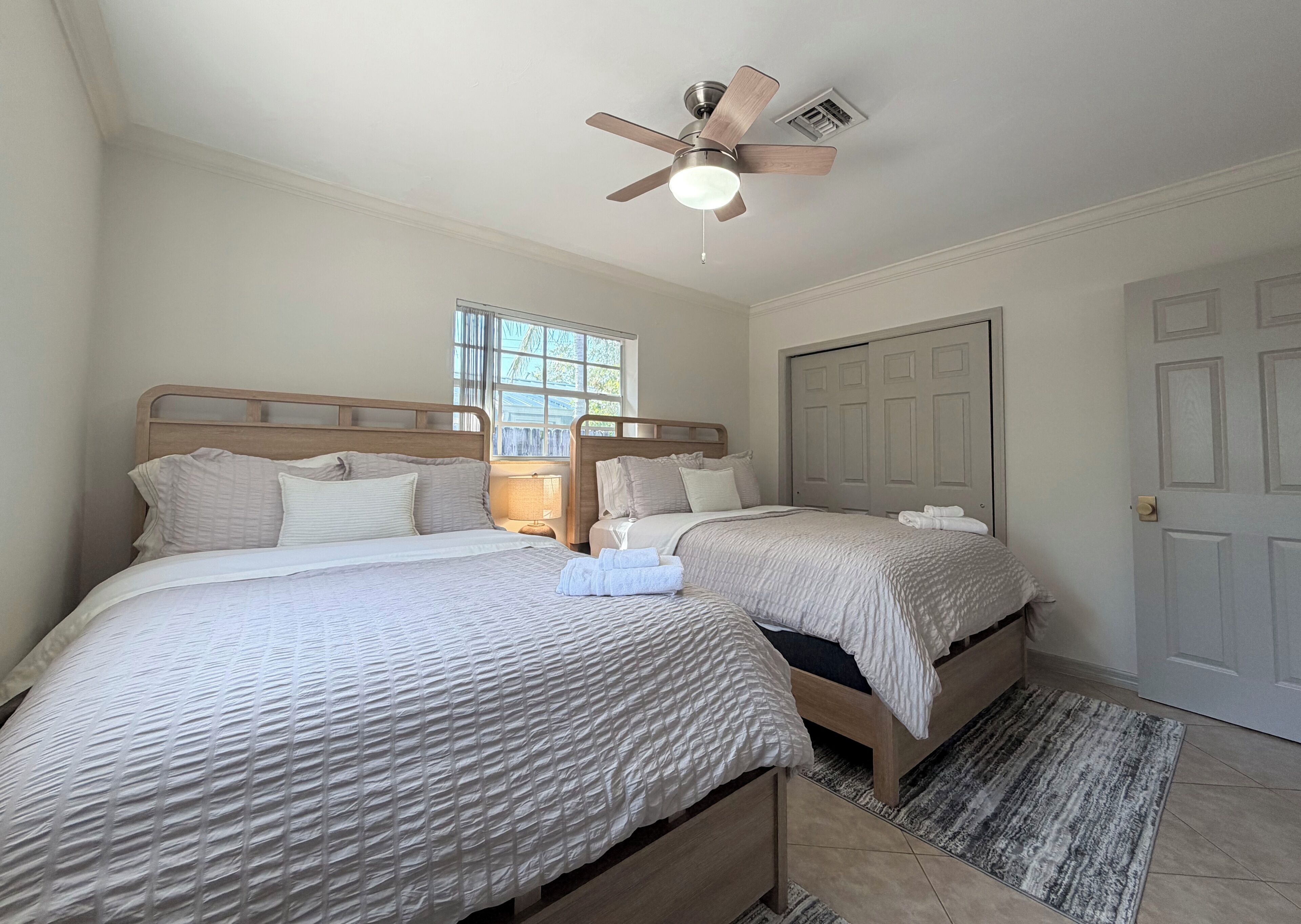 A bedroom with two beds, a ceiling fan, a window, and a door.