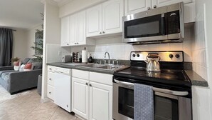 Une cuisine moderne avec des meubles blancs, un four à micro-ondes en acier inoxydable, un four et une bouilloire.
