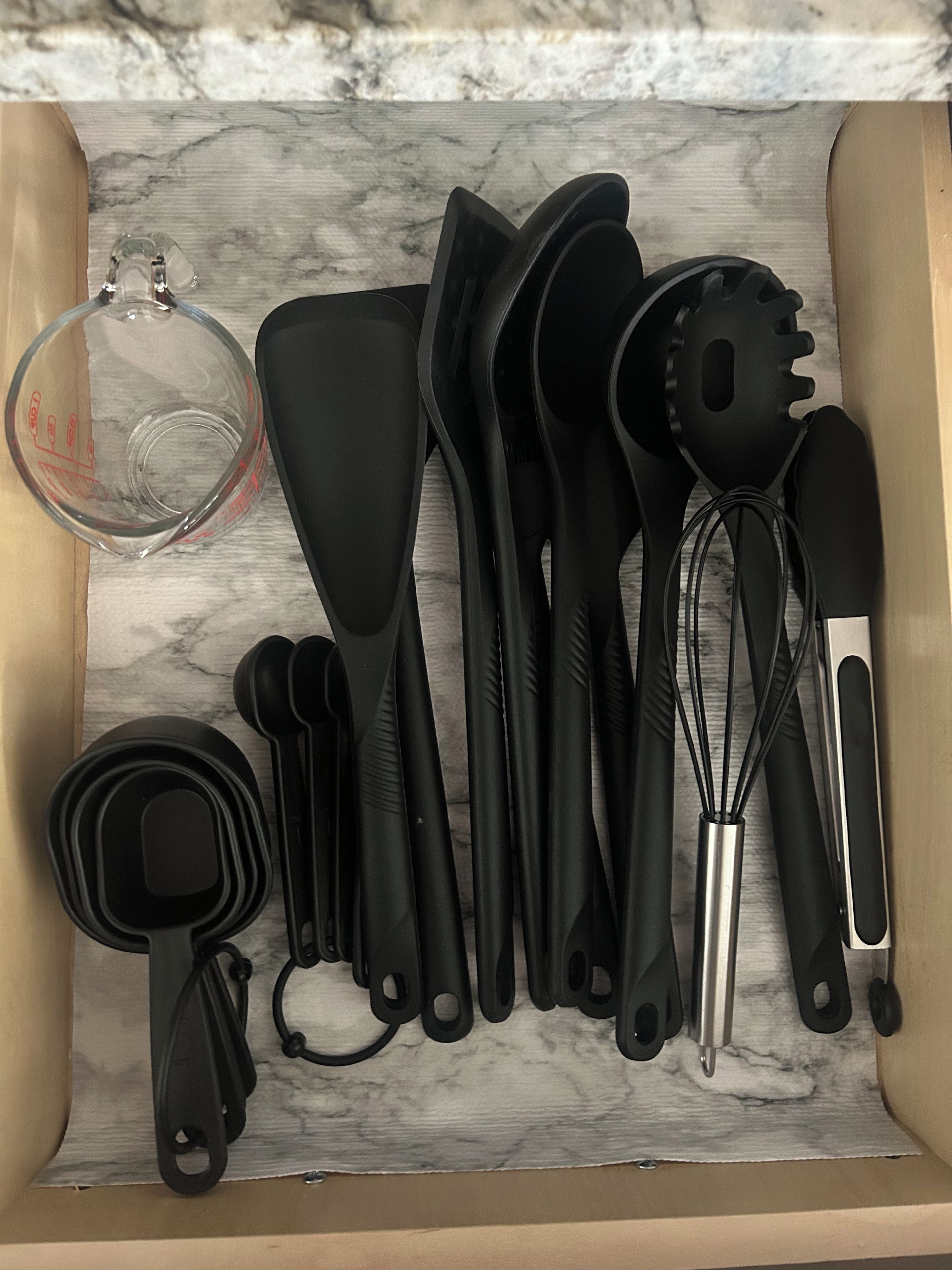 A drawer containing various kitchen utensils including a measuring cup, spatulas, a whisk, and a ladle.