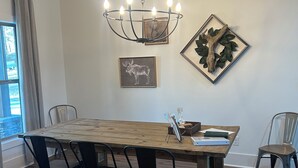 A dining area with a wooden table, black chairs, a chandelier, and framed artwork on the walls. - Driftwood Lodge on Lake Harding - On Quiet Cove with Kayaks and more (Valley)