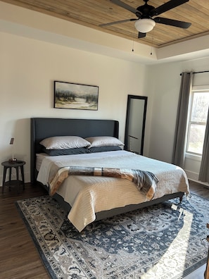 Une chambre à coucher avec un lit, un ventilateur de plafond, un tableau, une fenêtre avec des rideaux et un tapis.