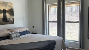 A bedroom with a bed, a ceiling fan, a window with curtains, and a painting on the wall. - Driftwood Lodge on Lake Harding - On Quiet Cove with Kayaks and more (Valley)