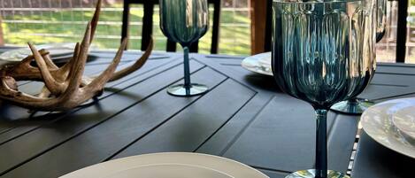 A dining table with plates and wine glasses, set outdoors with a view of trees.