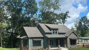 A two-story house with a stone exterior, a front porch, and a driveway.