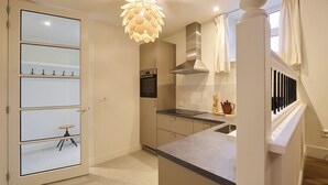 A modern kitchen with a built-in oven, a stainless steel range hood, and a unique pendant light.