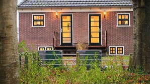 A brick house with a tiled roof, two large windows with black frames, and a door with a glass panel.