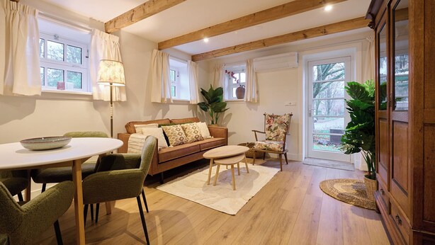 A cozy living room with a wooden ceiling, a brown sofa, a round table, and green chairs.