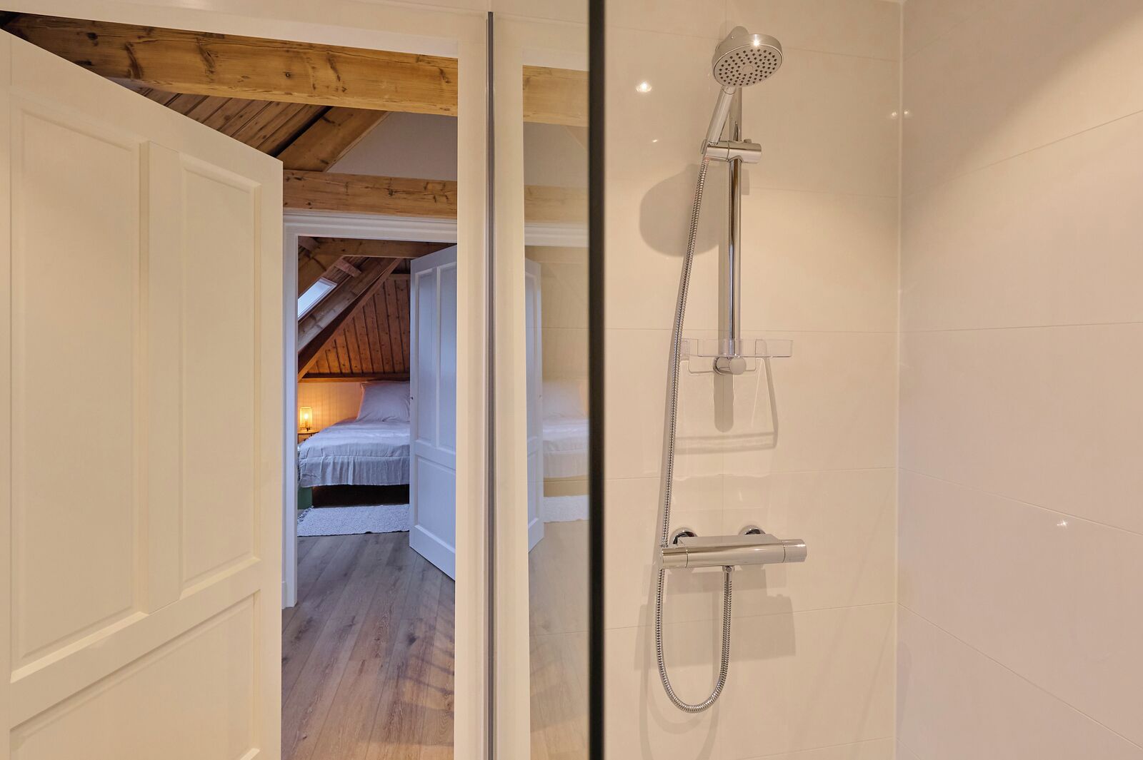 Une salle de bain moderne avec une douche à l’italienne en verre, un plafond en bois apparent, et une chambre à coucher avec un plafond en pente et un lit.
