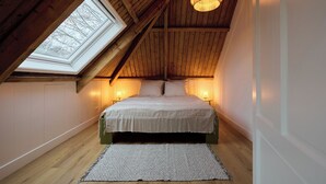 A bedroom with a sloped ceiling, a skylight, a bed, bedside lamps, and a rug.