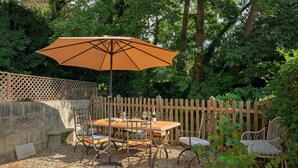 Eine Terrasse im Freien mit Tisch, Stühlen, Sonnenschirm und Holzlattenzaun.