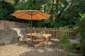 Eine Terrasse im Freien mit Tisch, Stühlen, Sonnenschirm und Holzlattenzaun.