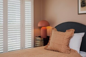 Une chambre à coucher avec un lit, une table de chevet, une lampe et une fenêtre avec des stores.