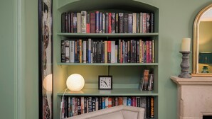 Ein Bücherregal mit verschiedenen Büchern, einer Uhr und einer Kerze auf einem Kaminvorsatz.