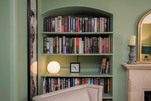 Ein Bücherregal mit verschiedenen Büchern, einer Uhr und einer Kerze auf einem Kaminvorsatz.