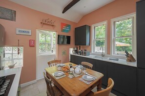 A kitchen with a dining table set for two, a television mounted above the counter, and a view of the outdoors through the windows. - Perfect location for city and countryside (Batheaston)