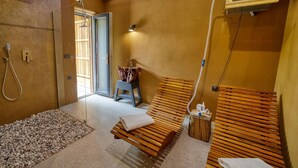 Een spa-ruimte met een houten bankje, een douchegedeelte en een klein tafeltje met handdoeken.