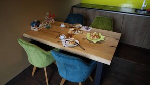 Een eethoek met een houten tafel, twee stoelen en een stoel in blauw-groen. Op tafel staat een vaas met bloemen, een bord met eten en een beker.