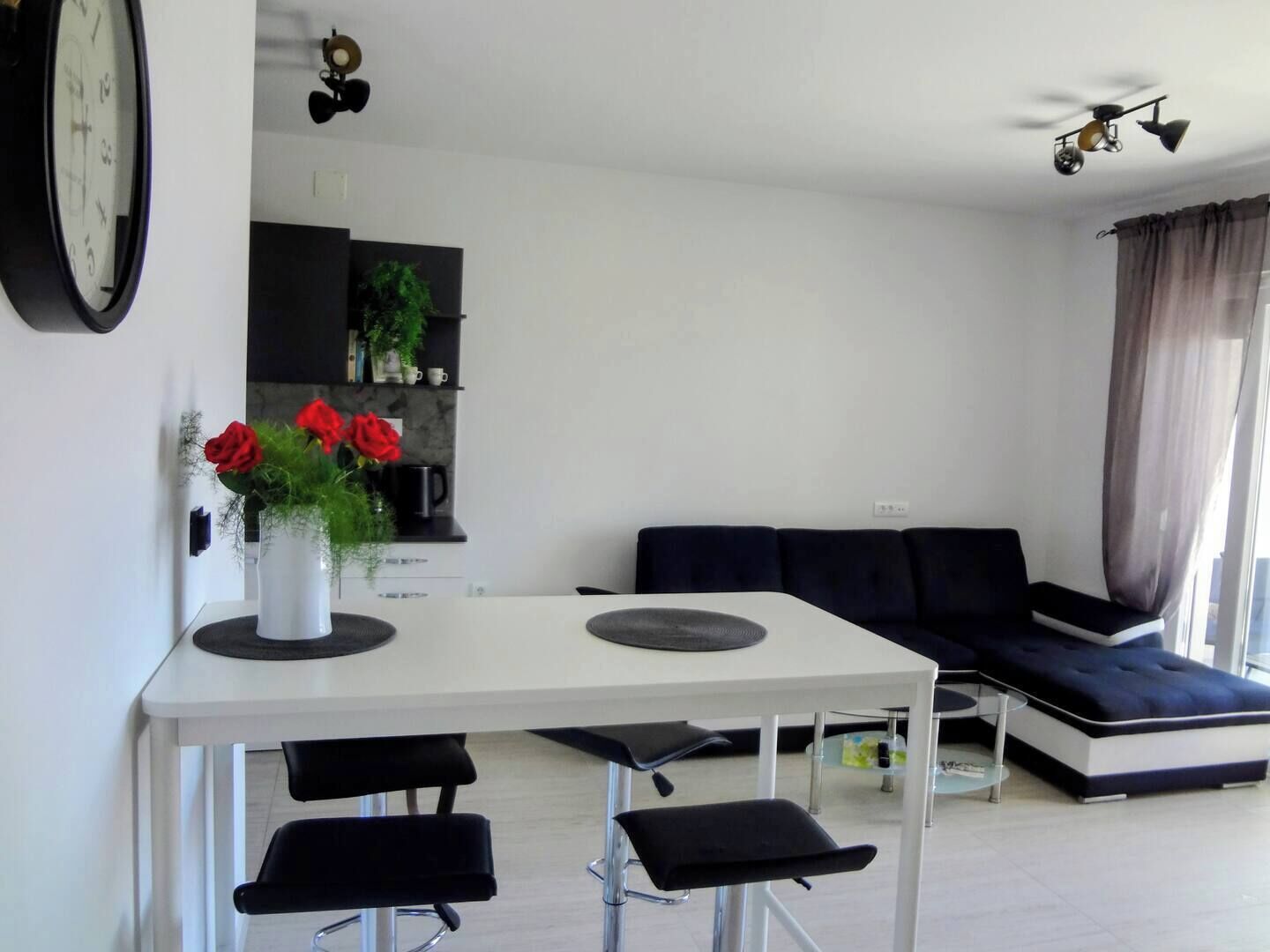 A modern living space with a white dining table, black chairs, a dark blue sofa, and a ceiling fan.