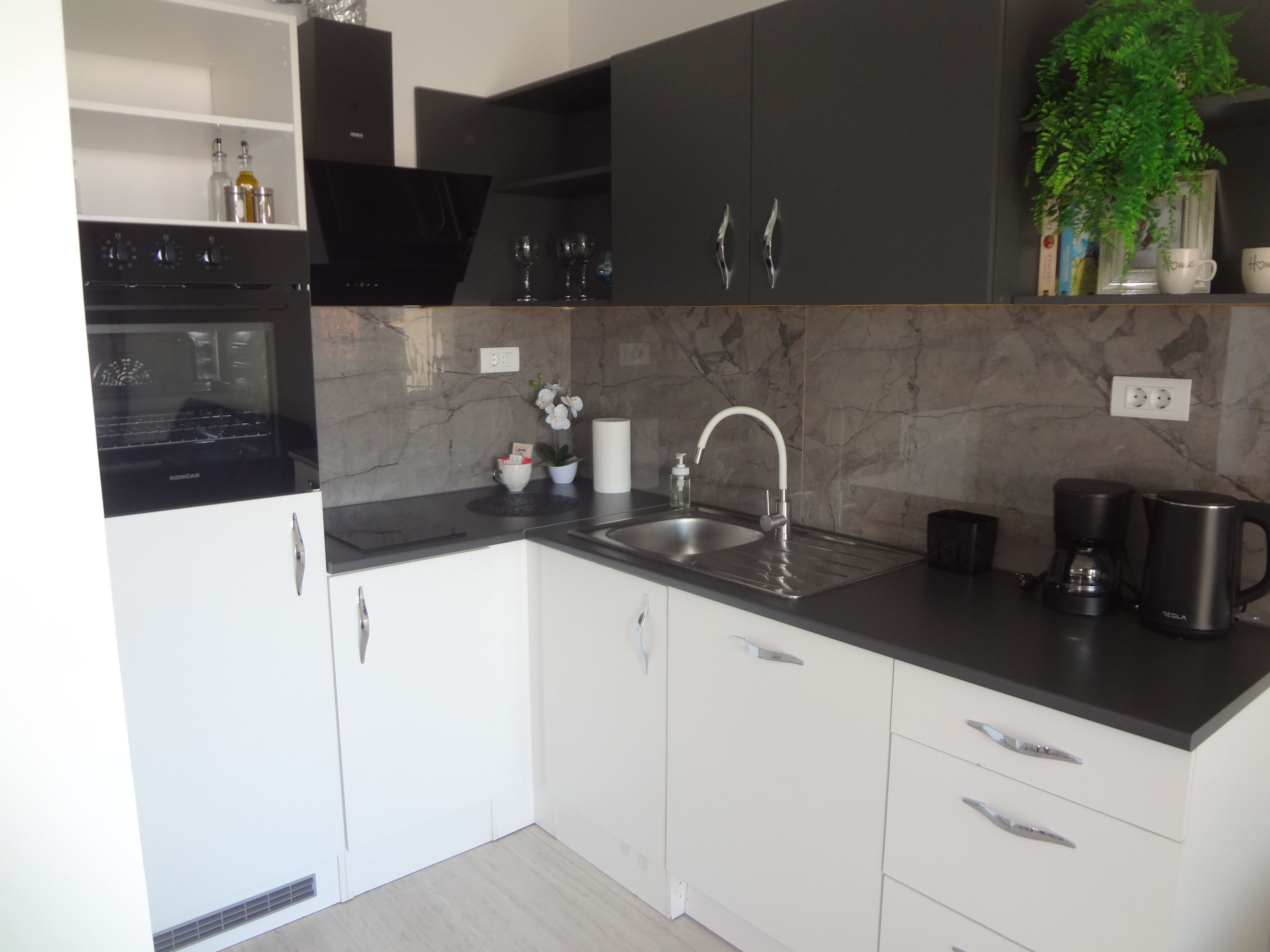 A modern kitchen with white cabinets, a black countertop, a stainless steel sink, and a coffee maker.