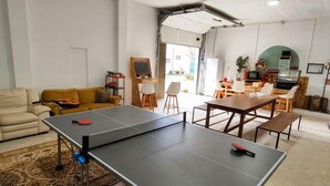 A ping pong table in a room with a sofa, chairs, and a coffee machine.
