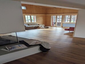 A spacious room with wooden floors, a sofa, and a red chair. - Baren Penthouse by Interhome (Zweisimmen)