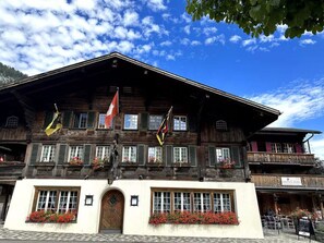 A traditional wooden building with multiple windows, a central entrance, and flags. - Baren Penthouse by Interhome (Zweisimmen)