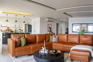 A modern living room with a brown leather sofa, a black coffee table, and a kitchen in the background.