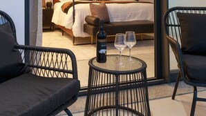 A modern bedroom with a four-poster bed, a small round table with a bottle and glasses, and two black chairs.